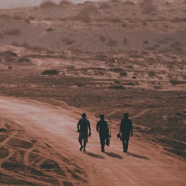 A US army medic assisting a soldier in a desert environment. The scene is dusty, with visible signs of military activity. The focus is on the care and support provided in challenging environmental conditions.